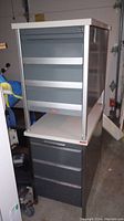 Photo showing stacked configuration of two TAB metal office drawer cabinets in a garage area, highlighting their size and overall condition.