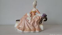 Full side view of the porcelain Royal Doulton figurine 'Reverie' showing the seated woman in peach gown with chaise lounge.
