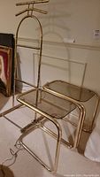Two brass colored metal framed smoked glass top side tables displayed with brass colored metal clothes butler with bamboo pattern edge.