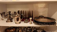 One shelf with silver plated items including two five-arm candle holders, a silver pitcher, a jigger, an envelope holder, and two trays.