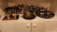Full shelf view showing full Viking Plate silver plated tea and coffee service with tray, large bowl, coffee pot, cream and sugar containers, and silver overlay bowl with holder.