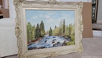 Frontal photo showing the entire framed acrylic landscape painting depicting a river and trees.