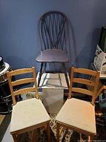 One purple Windsor-style chair with spindle back and seat along with two wooden ladder-back chairs with white fabric seats placed on a carpet.