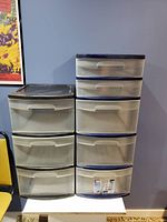 Two plastic rolling storage bins with multiple drawers placed side by side against a blue wall.