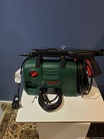 Front view showing Bosch EasyAquatak 1200 power washer with power cable and spray gun attached.