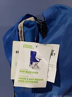 Blue carry bag with drawstring containing the folded camp chair, showing the product tag indicating it is an Everyday Essentials Outdoor High-Back Chair.