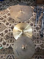 Photo showing three Pearl cymbals on a carpet, two have worn finish, one is shiny and brass-colored.
