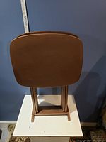 Three brown rectangular plastic trays stacked vertically on a foldable stand against a blue wall.