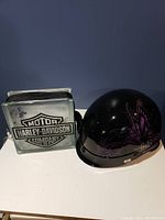 Black Harley-Davidson helmet with purple flame graphics and Harley-Davidson frosted glass logo lamp block side by side on a flat surface.