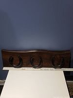 Front view of wooden coat rack with three black horseshoe hooks, placed against dark wall.