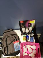 Photo showing entire lot with smart bulbs box, several loose bulbs, Philips bulbs, unopened lens covers, and grey Tracer backpack.