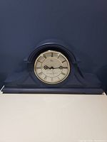 Front view of the blue mantle clock showing the circular clock face with Roman numerals.