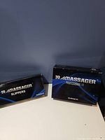 Boxed Massage Slippers and Massager Professional II device packaging side by side on floor against wall.