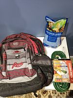 Mixed lot with backpack, aquarium gravel bag, and Woods extension cord combo pack arranged against blue backdrop.