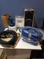 Full lot showing blue spray gun with paint container, black hose, user manual, black nozzles, and blue pump unit on white surface