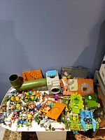 Overview shot of the entire lot on a white table showing multiple figures, vehicles, and sewer playset parts