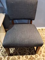 Front view of the gray fabric upholstered chair showing padded seat and backrest along with wooden legs