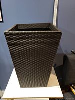 Full view of tall brown wicker planter with synthetic weave and plastic inner liner.
