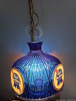 Front view of the blue plastic hanging lamp with Pabst Blue Ribbon logos illuminated.
