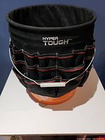 Black Hyper Tough tool wrap fitted around an orange bucket, showing multiple exterior pockets and metal handle.