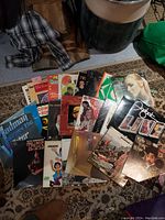 Photo showing an assortment of vintage vinyl records arranged in a pile on a patterned carpet with some partially visible titles and cover art.