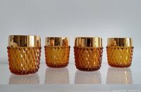 Front view of four amber-colored glass tumblers with diamond textured design and gold rim.
