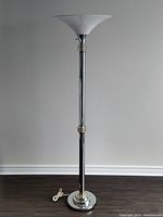 Full view of the tall chrome torchiere floor lamp with white acrylic flared shade and round chrome base.