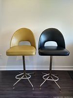 Front-facing view of the pair of vintage vinyl swivel bar stools with mustard yellow and black upholstery on metal bases.