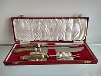 Open original red leatherette storage case showing carving knife, fork, and sharpening steel with antler handles in fitted slots