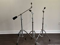 Three heavy duty cymbal stands with tripod legs and rubber feet on a wood floor against a wall