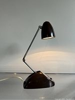 Front angled view of the lamp turned on showing light emission and shape of the conical shade and triangular base with switch.