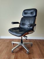 Front view showing black leather seat and backrest, walnut plywood sides and aluminum base with casters