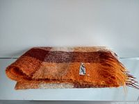 Folded orange, brown, and cream checkered mohair throw blanket with label visible
