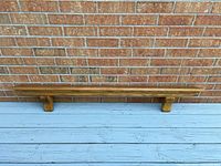Photo showing the full oak mantle resting against a brick wall and blue wooden floor, displaying the full length and supports underneath.