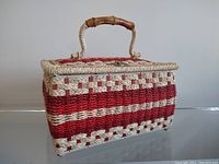 Full side view of a rectangular vintage woven sewing basket with red and cream pattern and bamboo handle.