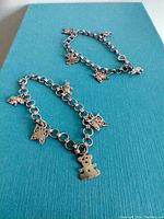 Pair of silver charm bracelets with multiple charms including teddy bear, butterfly, flower, and unicorn shapes.