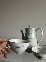 Close-up of teacup held showing delicate handle, butterfly pattern, and gold rim.