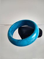 Turquoise bangle bracelet resting on a stand, showing its rounded shape and veining detail.