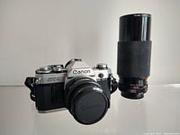 Front angle of Canon AT-1 camera with 50mm lens attached and telephoto lens standing beside it.