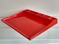 Red plastic desk organizer with slanted surface and multiple compartments shown on a white surface.