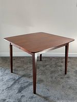 Angled full view of walnut dining table showing tapered legs and square top.