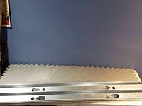 Four long metal studs stacked side by side on the floor against a wall.