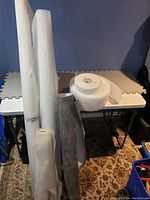 Shows multiple rolls of plastic vapor barrier sheets and foam insulation material standing against a table.