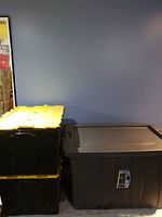 Photo showing two large plastic storage bins stacked, one with yellow lid and one with grey lid.