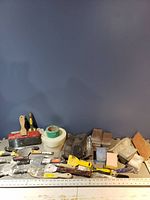 All drywall tools and supplies laid out showing putty knives, taping knives, sanding blocks, and rolls of mesh drywall tape.