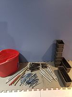 Overall view of all fasteners, plastic containers, and red bucket on foam mat against blue wall.