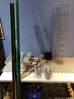 Fence lot items arranged on a table including green fence posts, wire fencing roll, metal brackets, and accessories.