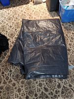 Folded large black tarp displayed on a patterned floor with visible grommeted edges.