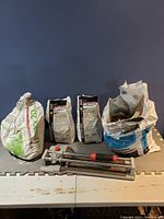 Four bags of grout and a manual tile cutter arranged together on a table.