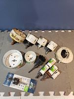 Hole saw bits and arbors arranged on a grey foam surface. Various sizes of bits with some showing wear and paint chipping. Includes a new arbor in packaging.